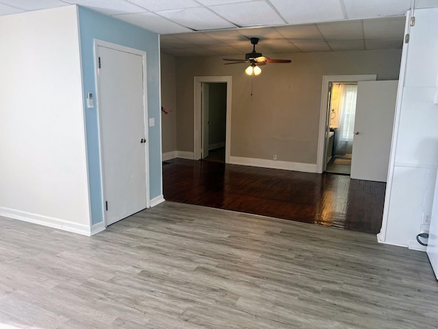 spare room with baseboards, ceiling fan, wood finished floors, and a paneled ceiling