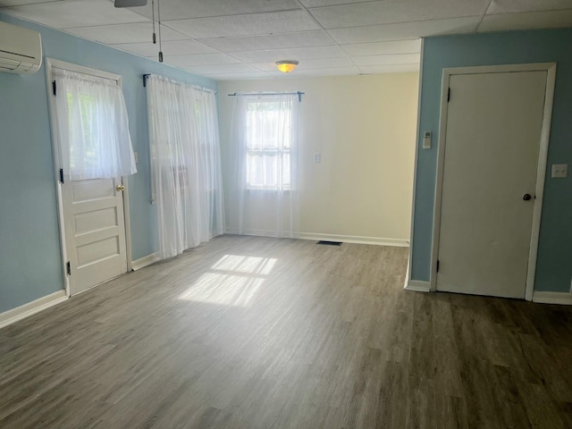 spare room featuring wood finished floors, a drop ceiling, a wall mounted AC, and visible vents
