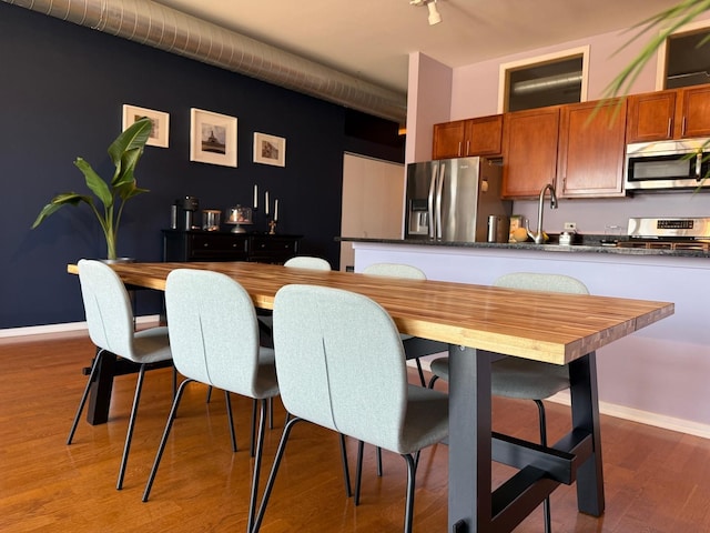kitchen featuring light wood-style flooring, a sink, brown cabinets, dark countertops, and stainless steel appliances