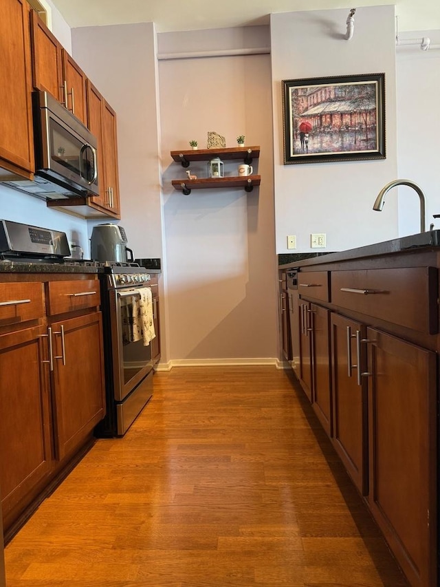 kitchen featuring wood finished floors, open shelves, stainless steel appliances, brown cabinetry, and baseboards