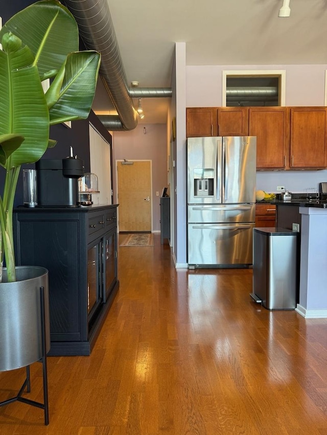 kitchen with brown cabinets, dark countertops, stainless steel fridge with ice dispenser, and dark wood-type flooring