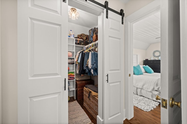 walk in closet featuring wood finished floors, a barn door, and lofted ceiling