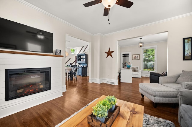 living area featuring ornamental molding, a glass covered fireplace, wood finished floors, a ceiling fan, and baseboards