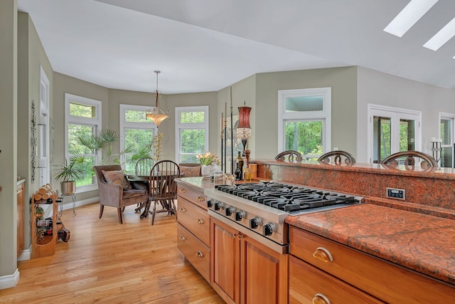 kitchen featuring a skylight, stainless steel gas cooktop, brown cabinetry, light wood-style floors, and pendant lighting