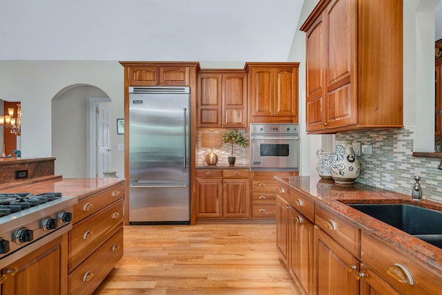 kitchen with stainless steel appliances, arched walkways, brown cabinets, and stone countertops