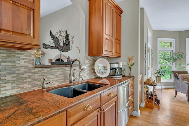 kitchen featuring a sink, dishwasher, dark stone counters, light wood-style flooring, and tasteful backsplash