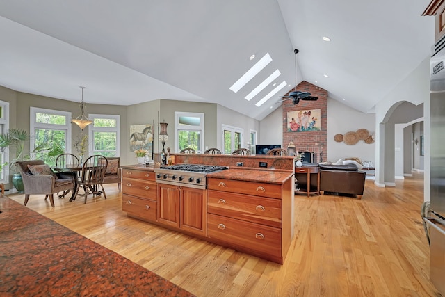 kitchen with light wood-style floors, a fireplace, stainless steel gas stovetop, brown cabinetry, and arched walkways