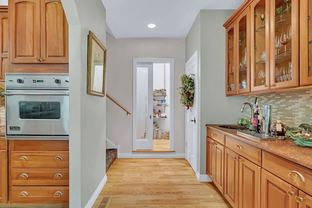 kitchen featuring oven, a sink, tasteful backsplash, light wood-style flooring, and baseboards