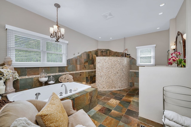 bathroom featuring stone tile flooring, a garden tub, a walk in shower, a chandelier, and recessed lighting
