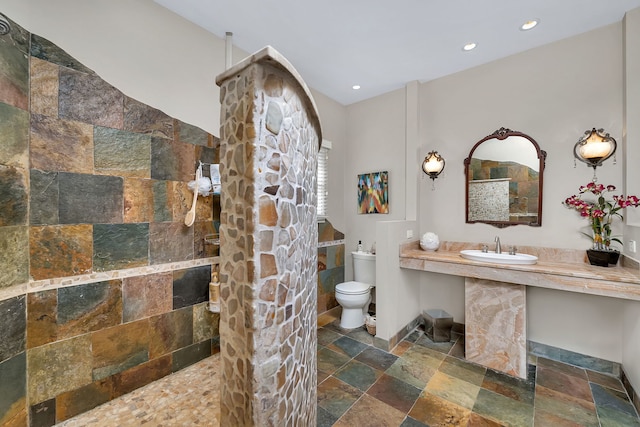 bathroom with stone tile flooring, a walk in shower, a sink, toilet, and recessed lighting