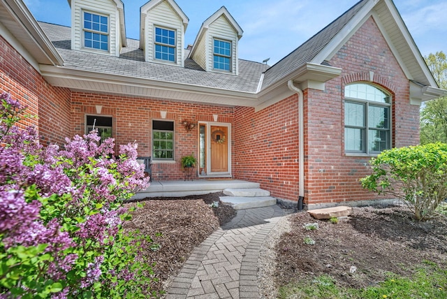 view of exterior entry with brick siding, roof with shingles, and a porch