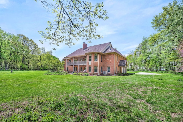 rear view of property with brick siding, a chimney, a yard, and a balcony