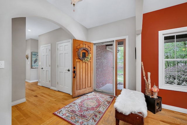 foyer entrance with arched walkways, plenty of natural light, light wood-style flooring, and baseboards