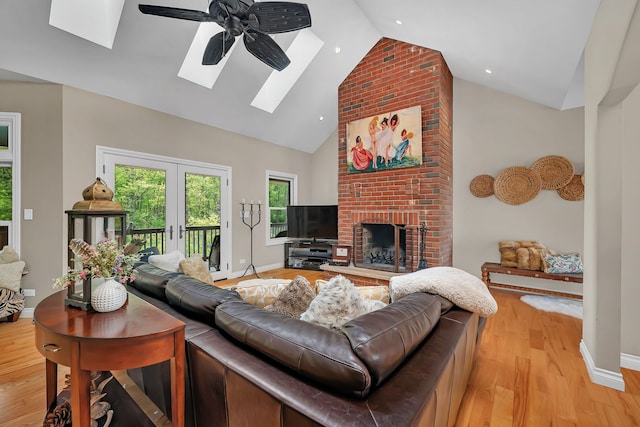 living room with a skylight, high vaulted ceiling, a brick fireplace, baseboards, and french doors