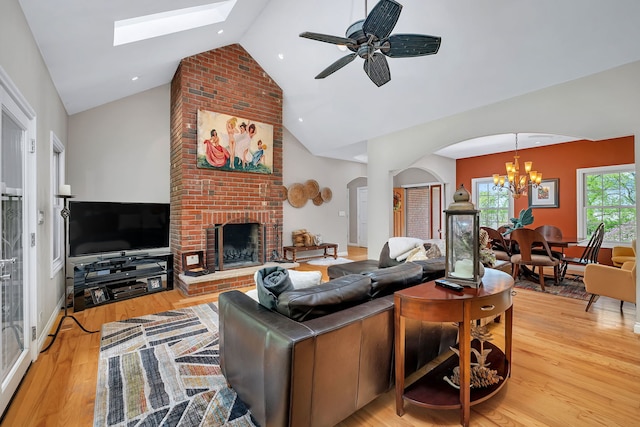 living room with arched walkways, high vaulted ceiling, a brick fireplace, light wood finished floors, and a chandelier
