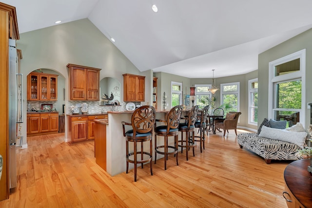 kitchen with a breakfast bar area, brown cabinetry, light wood finished floors, backsplash, and high vaulted ceiling