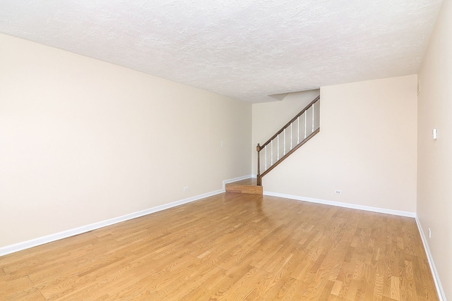unfurnished living room featuring light wood-style flooring, baseboards, stairway, and a textured ceiling