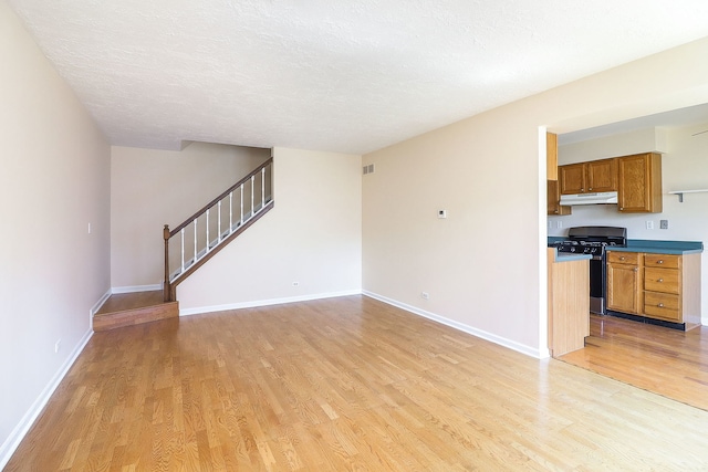 unfurnished living room featuring light wood-style floors, stairway, baseboards, and a textured ceiling