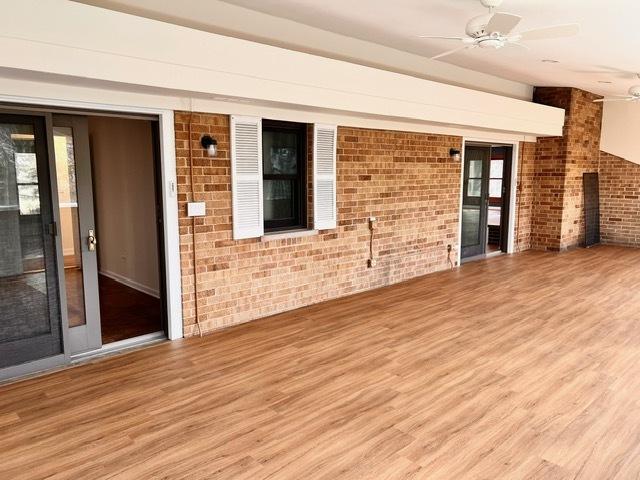 empty room with a ceiling fan, brick wall, and wood finished floors