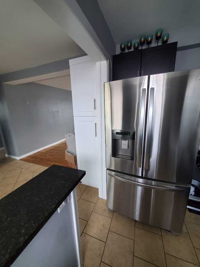 kitchen featuring baseboards, dark stone counters, light tile patterned flooring, and stainless steel refrigerator with ice dispenser