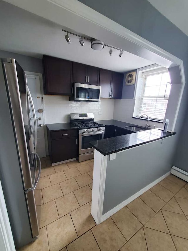 kitchen featuring a sink, a peninsula, stainless steel appliances, light tile patterned floors, and dark countertops