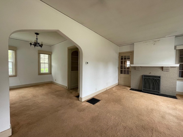 unfurnished living room featuring arched walkways, carpet flooring, a chandelier, a fireplace, and baseboards