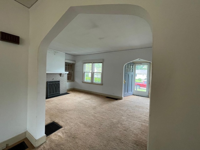 unfurnished living room featuring arched walkways, carpet flooring, a fireplace, and baseboards