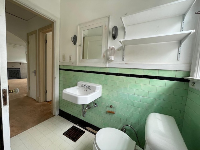 half bath with a sink, tile walls, toilet, and a wainscoted wall