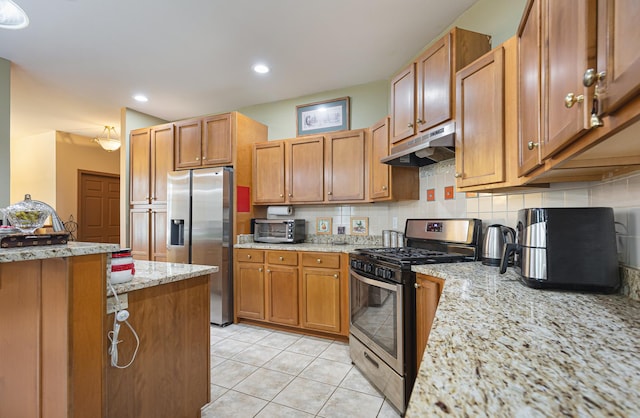 kitchen with a toaster, under cabinet range hood, light tile patterned floors, stainless steel appliances, and tasteful backsplash