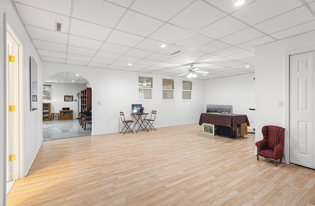 sitting room with light wood-type flooring, a ceiling fan, arched walkways, and a paneled ceiling