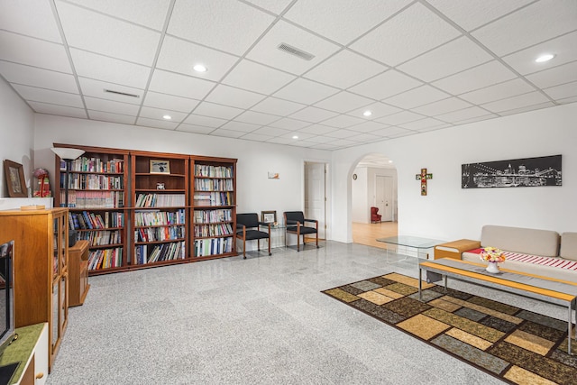 living area featuring a drop ceiling, granite finish floor, visible vents, arched walkways, and recessed lighting