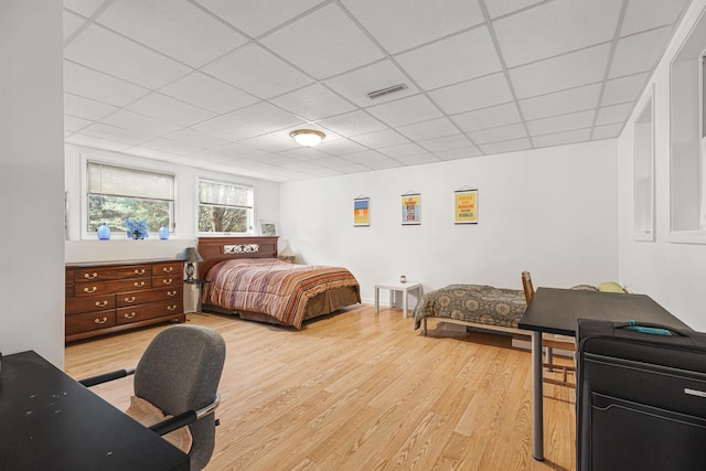 bedroom with light wood-type flooring, a drop ceiling, and visible vents