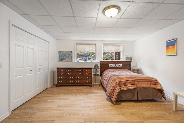 bedroom featuring a closet, a drop ceiling, light wood-style flooring, and baseboards