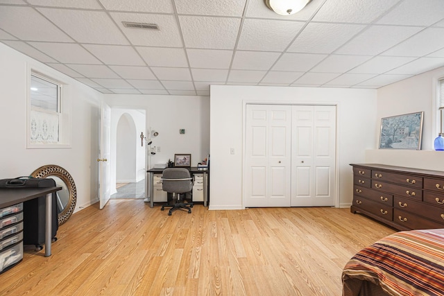bedroom with light wood-type flooring, a drop ceiling, visible vents, and arched walkways