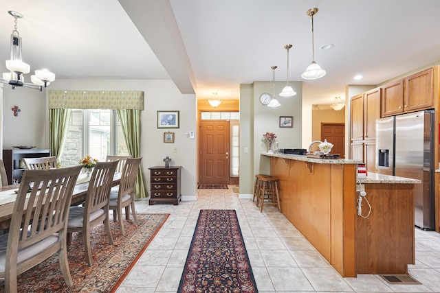 kitchen with a peninsula, brown cabinets, a breakfast bar area, light stone countertops, and stainless steel fridge with ice dispenser
