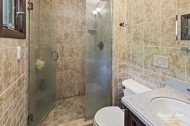 bathroom with tile walls, toilet, a stall shower, and vanity