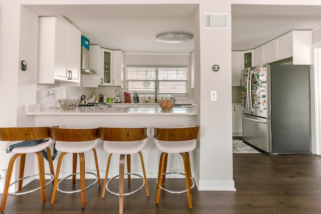 kitchen with glass insert cabinets, a breakfast bar, visible vents, white cabinetry, and stainless steel refrigerator with ice dispenser