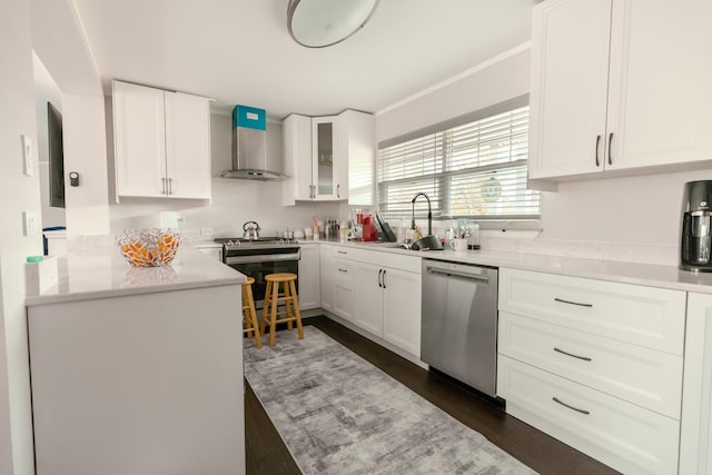 kitchen featuring stainless steel appliances, a sink, wall chimney range hood, light countertops, and white cabinets