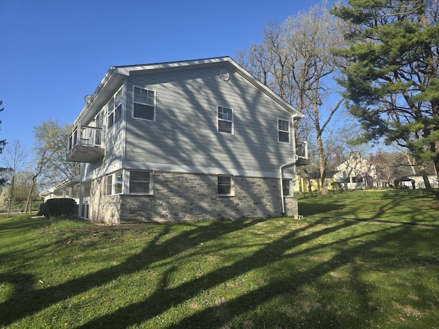 view of side of property featuring a yard, brick siding, and a balcony