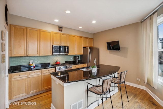 kitchen featuring a sink, stainless steel appliances, tasteful backsplash, light wood-type flooring, and visible vents