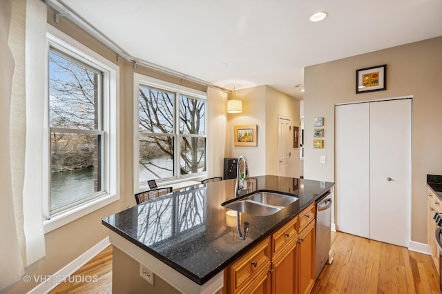 kitchen featuring a kitchen island with sink, dishwasher, light wood-style flooring, and a sink