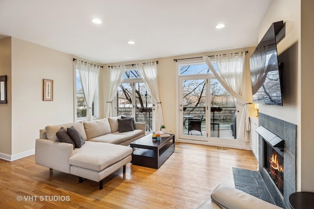 living area featuring baseboards, recessed lighting, light wood-style flooring, and a fireplace with flush hearth