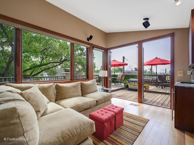 living area featuring a wealth of natural light, light wood finished floors, visible vents, and vaulted ceiling