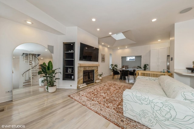 living room featuring a premium fireplace, light wood finished floors, visible vents, stairway, and a skylight