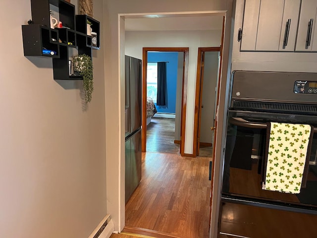 corridor with baseboards, baseboard heating, and wood finished floors
