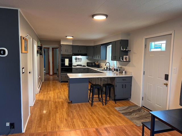 kitchen with black oven, a peninsula, extractor fan, stainless steel gas cooktop, and light countertops