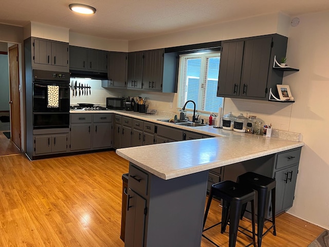kitchen with a peninsula, a sink, black appliances, a warming drawer, and under cabinet range hood