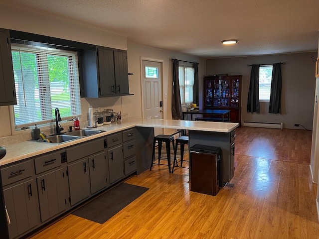 kitchen with light wood finished floors, light countertops, baseboard heating, and a peninsula