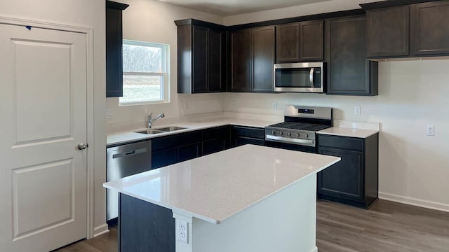 kitchen featuring baseboards, light stone counters, a sink, wood finished floors, and appliances with stainless steel finishes