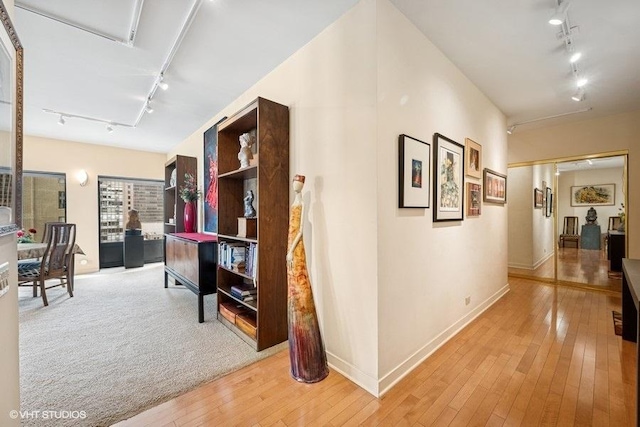 corridor with rail lighting, light wood-style flooring, and baseboards